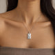 Modelka w dzianinowym topie bandeau w kolorze taupe z personalizowanym kwadratowym srebrnym naszyjnikiem z białymi cyrkoniami, z grawerem inicjałów i daty z przodu