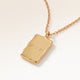 Close-up of a rectangular gold pendant with a soft melted look and personal engraving of initials with a heart on the polished back