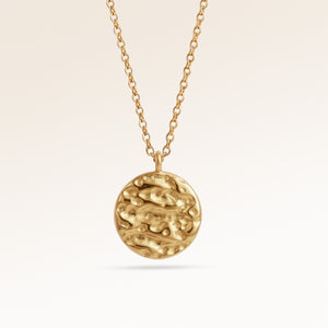 Close-up of minimalist round pendant in gold with softly melted finish and space for engraving on back