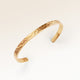 Close-up of minimalist bangle bracelet in gold with rippled wave surface and space for personalized engraving