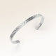 Close-up of minimalist bangle bracelet in silver with rippled wave surface and space for personalized engraving