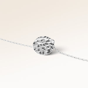 Close-up of minimalist round pendant in silver with rippled wave surface and space for engraving on back