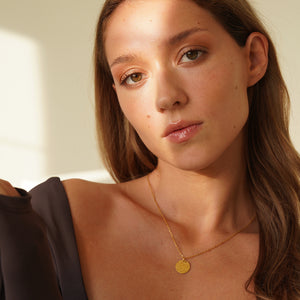 Personalized round gold necklace with rippled wave surface and space for engraving of text, coordinates or handwriting on the back
