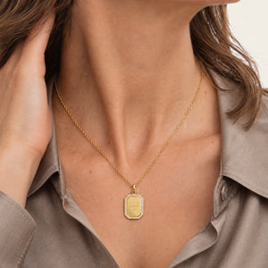 Model in a taupe satin shirt wearing a personalized octagonal gold necklace with white zircons along the edge and an engraved text and date on the front