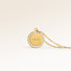 Close-up of minimalist round pendant in gold with white zircons along the edge and space for engraving on the front