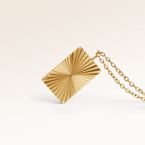 Close-up of minimalist square pendant in gold with ribbed sunburst surface and space for engraving on back