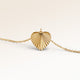 Close-up of minimalist heart pendant in gold with ribbed sunburst surface and space for engraving on the back.
