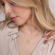 Model wearing personalized heart-shaped necklace for women in gold with ribbed sunburst pattern and engraving on back, from Mon Chou.