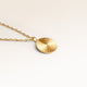 Close-up of minimalist round pendant in gold with ribbed sunburst surface and space for engraving on back