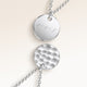 Close-up of two round pendants in silver – rippled front and polished back with an engraved initial